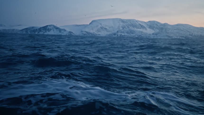 Dramatic slow-motion view of the choppy arctic ocean with stunning snow-covered mountains in the background