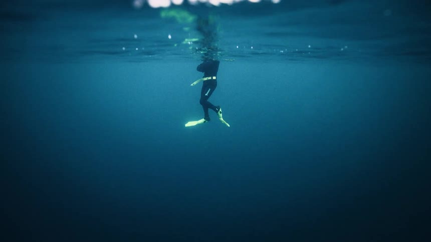 Underwater view of a diver in a wetsuit floating peacefully in the vast, deep blue sea