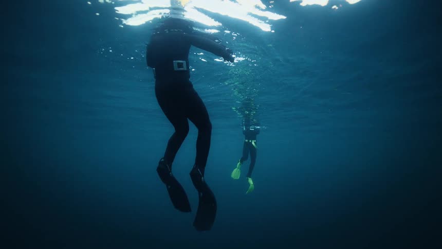 An underwater shot captures two divers in wetsuits floating at the surface of the vast, deep blue ocean