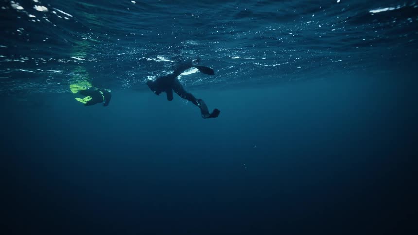 An underwater slow-motion view of three freedivers floating on the deep blue ocean surface