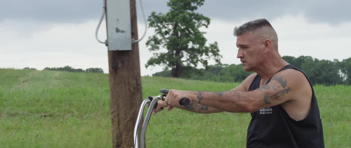 Tattooed man riding a bike past a green field