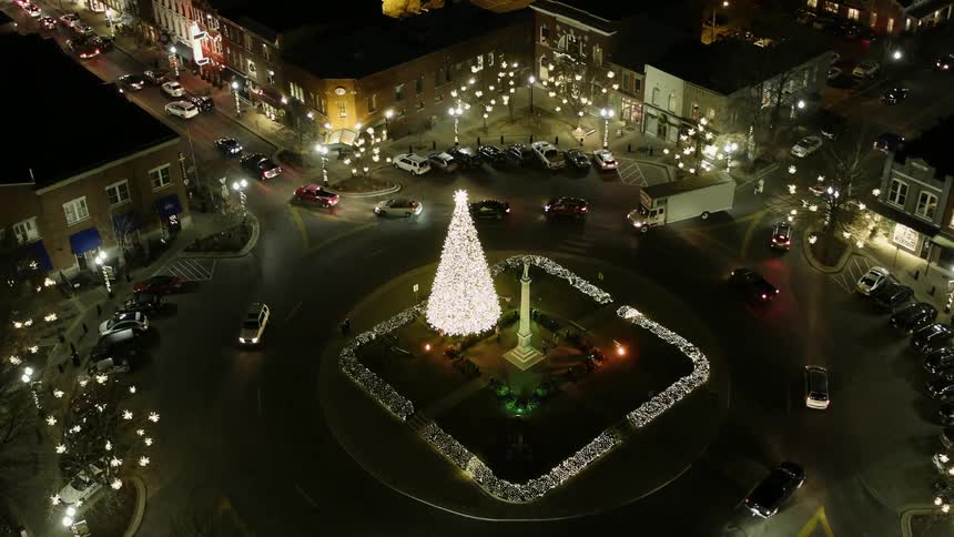 Cars drive around an illuminated christmas tree in a city