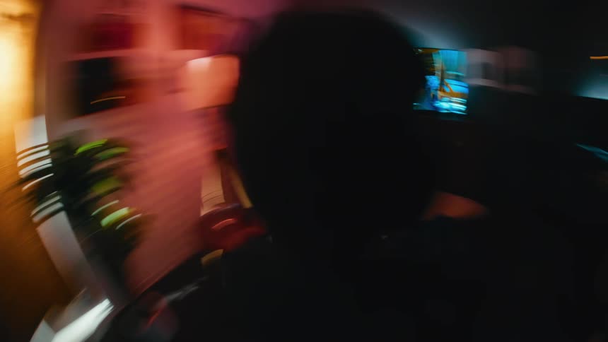 A dizzying, fast-spinning camera shot captures an intense gamer playing a video game in a dark, neon-lit room
