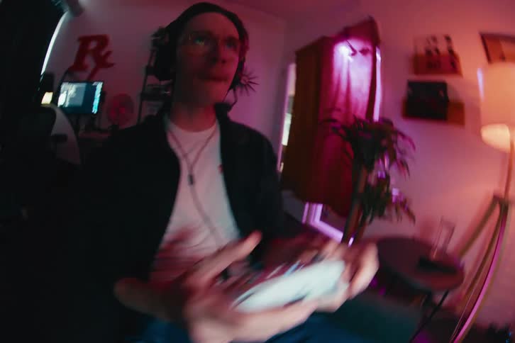 A young man wearing a headset gets excited and makes expressive faces while intensely playing a video game in a neon-lit room