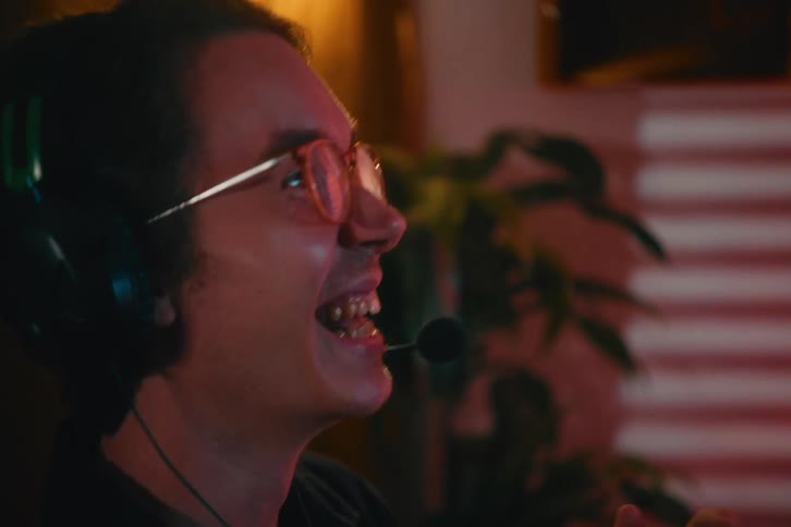 Close-up of a joyful gamer with glasses and a headset laughing enthusiastically while playing a video game in a warmly lit room