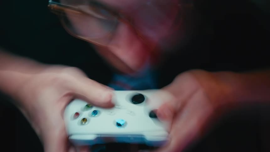 A disorienting close-up captures a focused gamer frantically using a white controller in a dark room