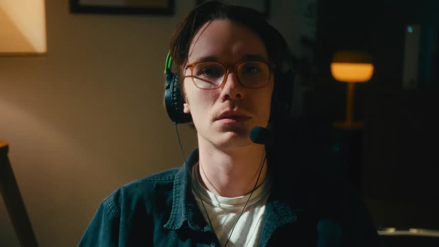 A slow tilt-up shot reveals a focused young gamer wearing glasses and a headset, holding a controller in a dimly lit room