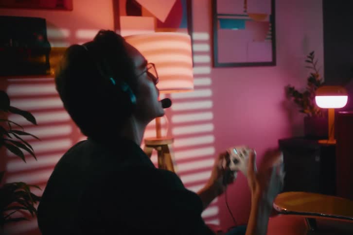 A passionate gamer with a headset emotionally reacts while playing a video game in a stylish, dimly lit room