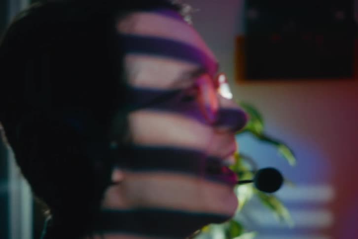Excited gamer wearing glasses and a headset laughs while playing a video game in a dark room with projected lights on his face