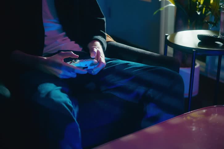 Close-up of a person's hands rapidly moving while playing a video game with a white controller in a dark room