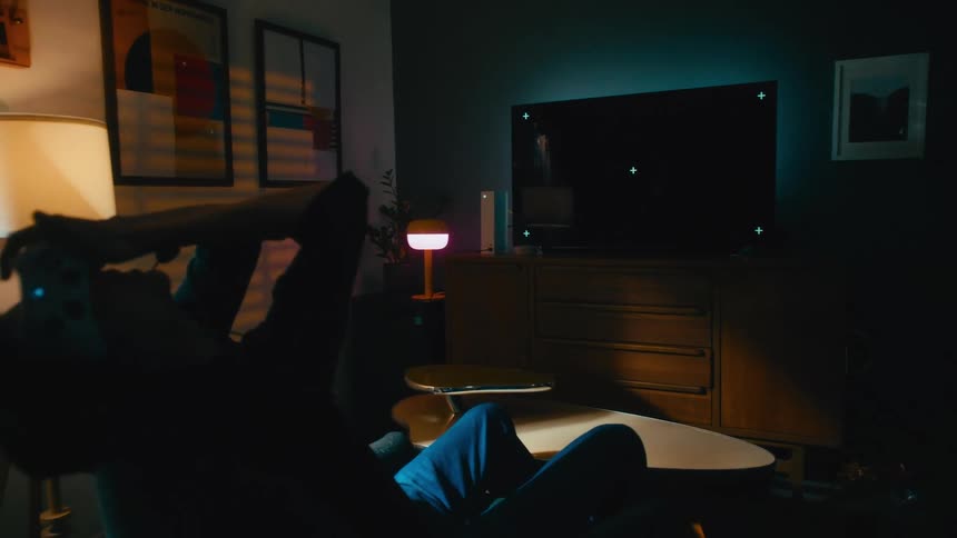 Frustrated gamer throws hands up in the air in anger after losing a video game on a TV with a chroma key green screen in a dark room at night