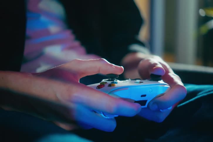 A close-up shot of a gamer's hands using the joysticks on a white controller, illuminated by colorful screen reflections