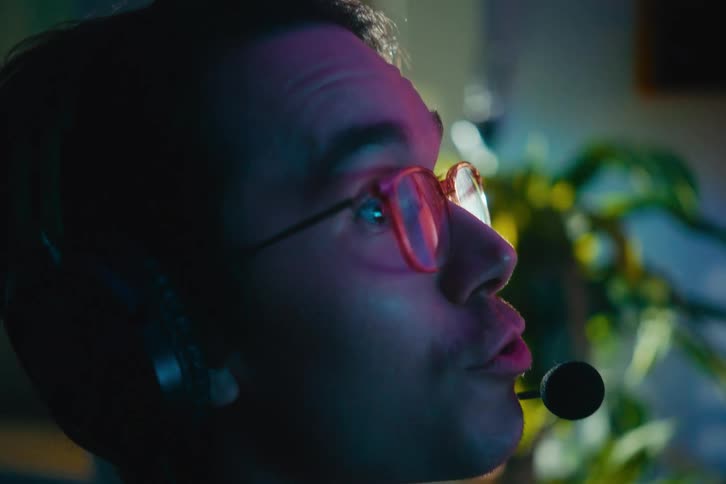 Close-up of an excited young man wearing a headset and talking while playing a video game in a neon-lit room