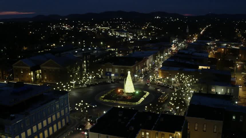 Cars travel in a roundabout with a lit christmas tree at its center