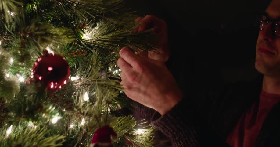 A man hangs an ornament on a christmas tree