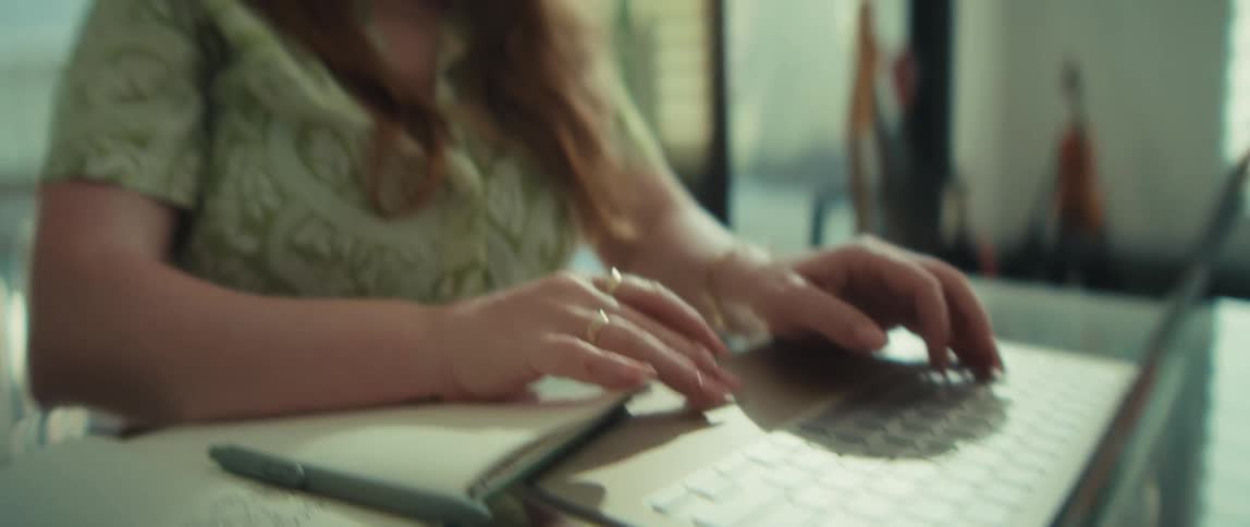 A close-up shot of a young businesswoman's hands typing on a laptop, tilting up to reveal her smiling face as she works