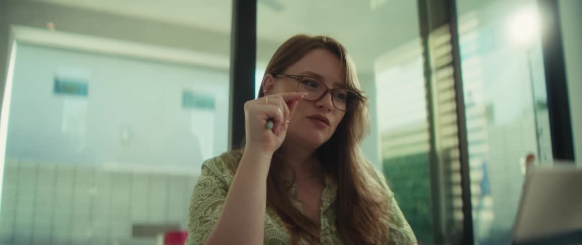 A thoughtful young woman with glasses concentrates while working on her laptop in a modern office