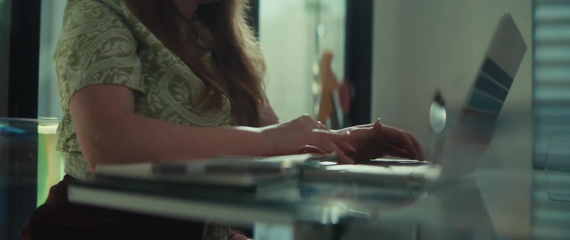 A woman types on a laptop keyboard at a glass desk in a home office setting