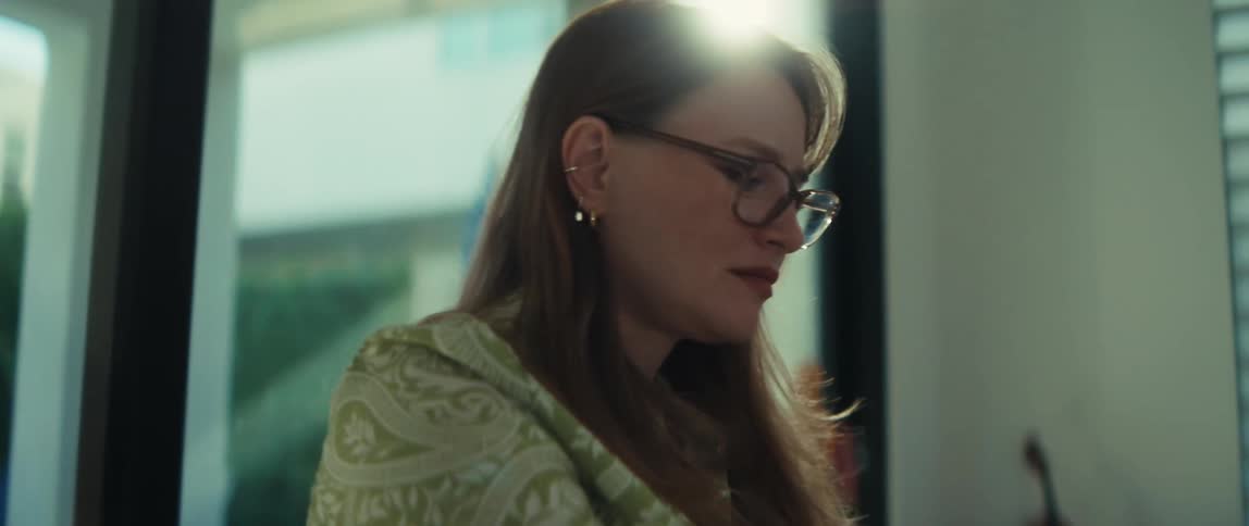 A woman with glasses types on her laptop at a desk, with the camera slowly zooming in for a close-up as she begins to smile