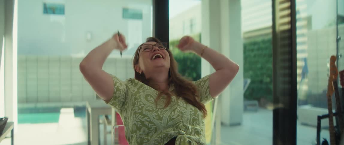 A happy woman in glasses working on her laptop from home celebrates her success with a joyful cheer in slow motion