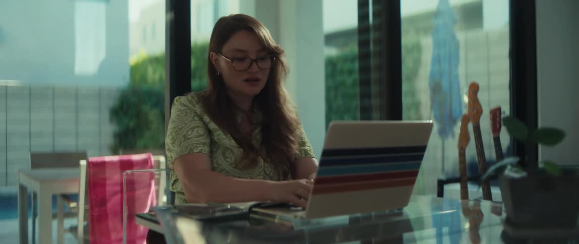 A focused woman with glasses types diligently on her laptop while working from her modern, sunlit home