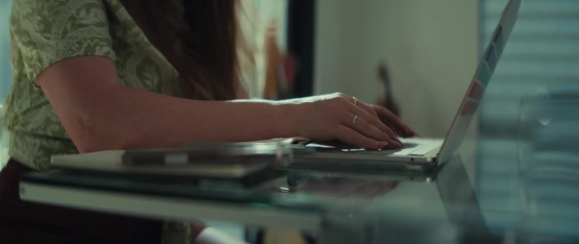 A focused businesswoman in glasses works diligently on her laptop in a sunlit office, the camera slowly panning down to her typing hands
