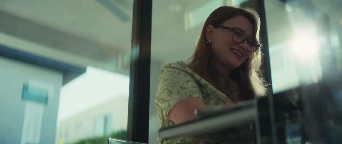 A slow motion close up of a joyful woman with glasses laughing while sitting in front of a window in her home