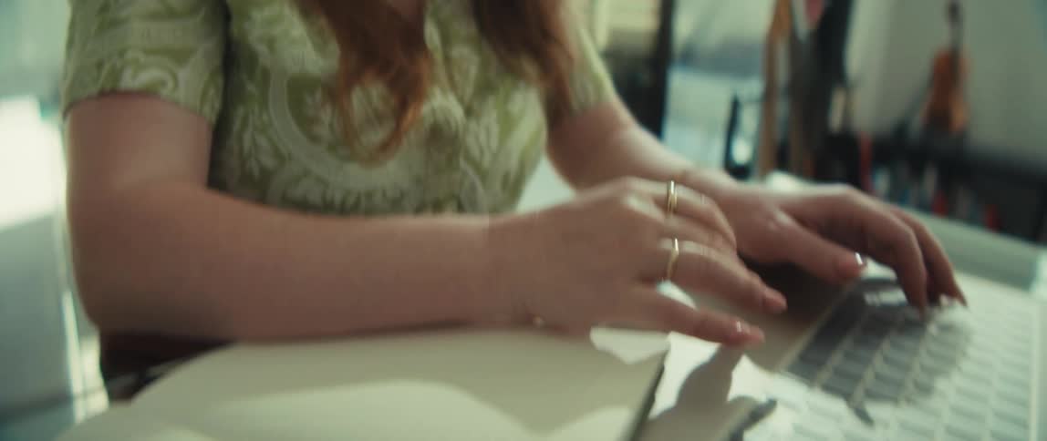 A close-up shot tilts down from a smiling woman's face to her hands typing on a laptop at a desk