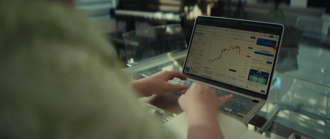Over-the-shoulder view of a person using a laptop to analyze stock market or cryptocurrency charts