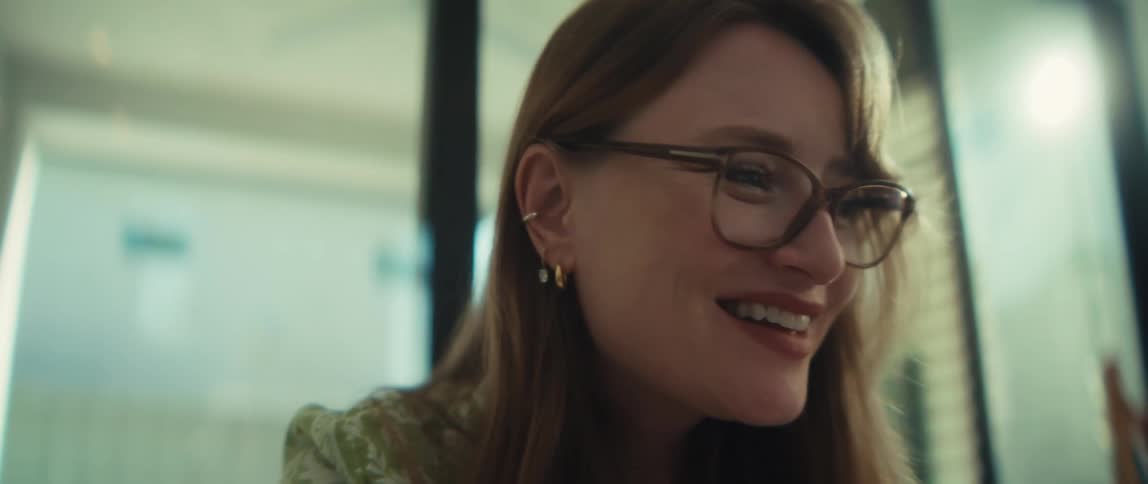 Close-up of a happy businesswoman in glasses, smiling with satisfaction while working on her laptop in a bright, modern office