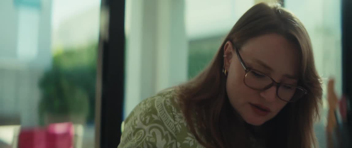 A close-up shot of a focused young woman with glasses, typing and working on her laptop in a sunlit room
