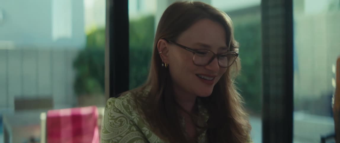 A woman in glasses works on her laptop at home, her expression shifting from focused concentration to a warm smile as the camera zooms in