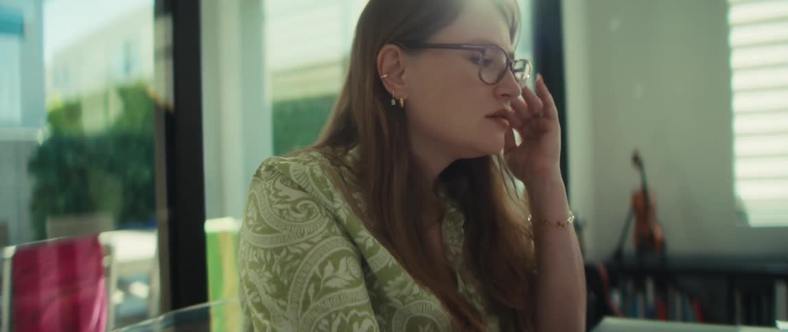 A concerned woman with glasses works on her laptop at a glass table, showing signs of stress and deep thought