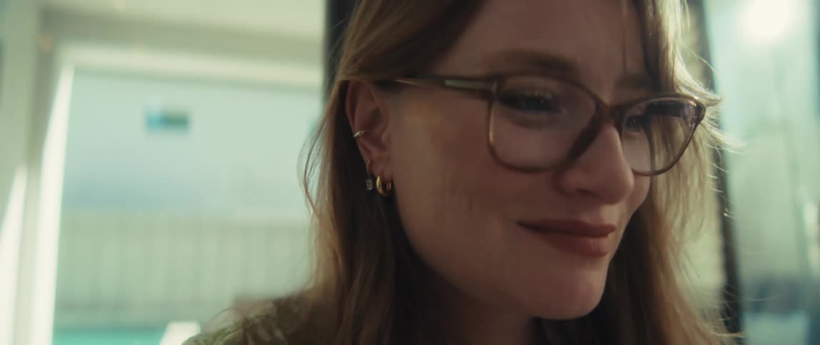 Close-up slow-motion shot of a woman with red hair and glasses typing on a laptop, with the camera tilting up to reveal her content smile