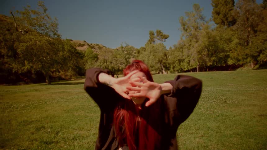 A woman with vibrant red hair performs a flowing, expressive dance in a sun-drenched park, her movements capturing a sense of artistic freedom