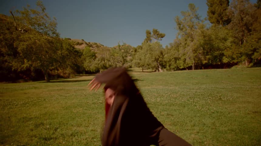 In slow motion, a woman with long red hair gracefully practices martial arts in a sunny, green park