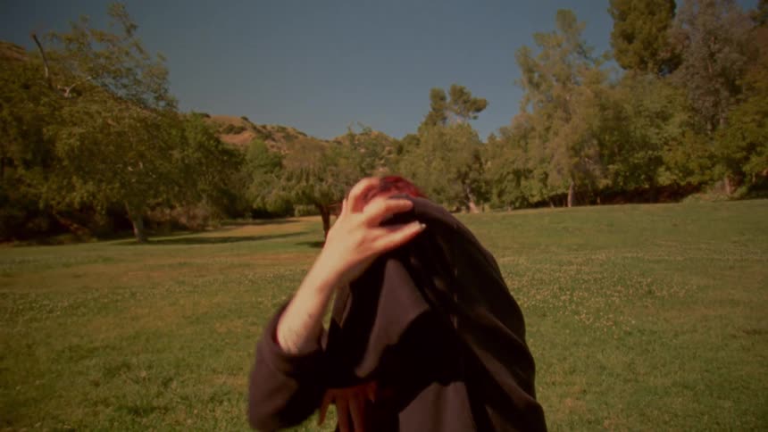 A woman with long red hair performs an expressive and contemporary dance in a sunny, green park