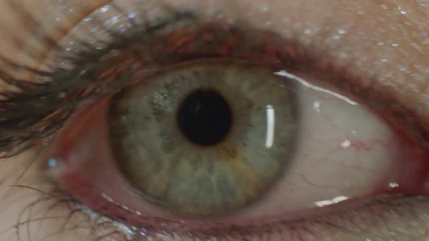 Intense macro shot of a blinking green eye adorned with shimmering glitter eyeshadow