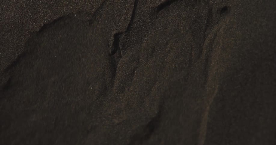 Fine black sand gently falls in slow motion, creating an abstract textural background