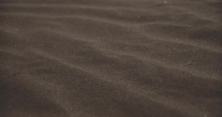 Wind gently blows sand over the ripples of a desert dune in a close-up shot