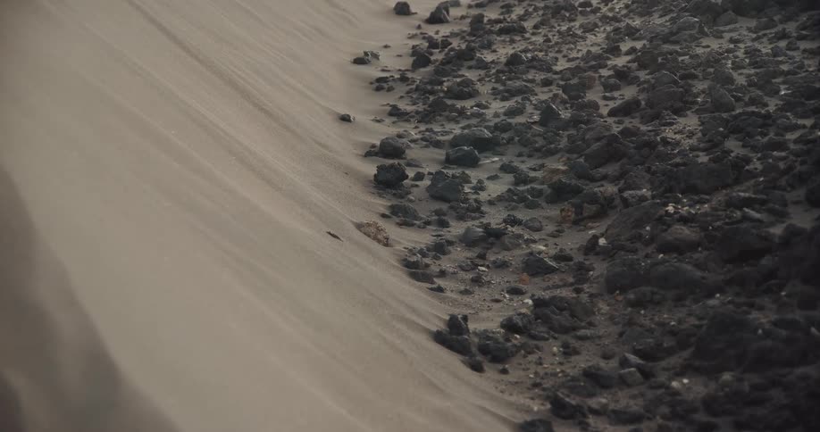 Close-up of sand blowing in the wind across a desolate landscape of dark volcanic rocks