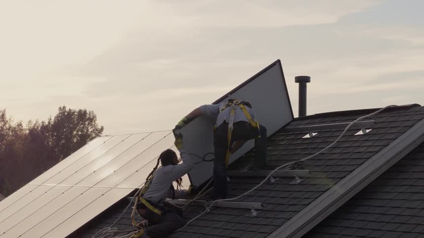 Workers install solar panels on a roof