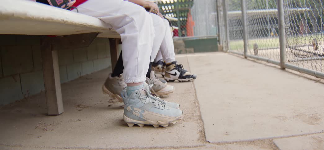 Low angle shot of young baseball players' feet and cleats as they nervously wait on the dugout bench