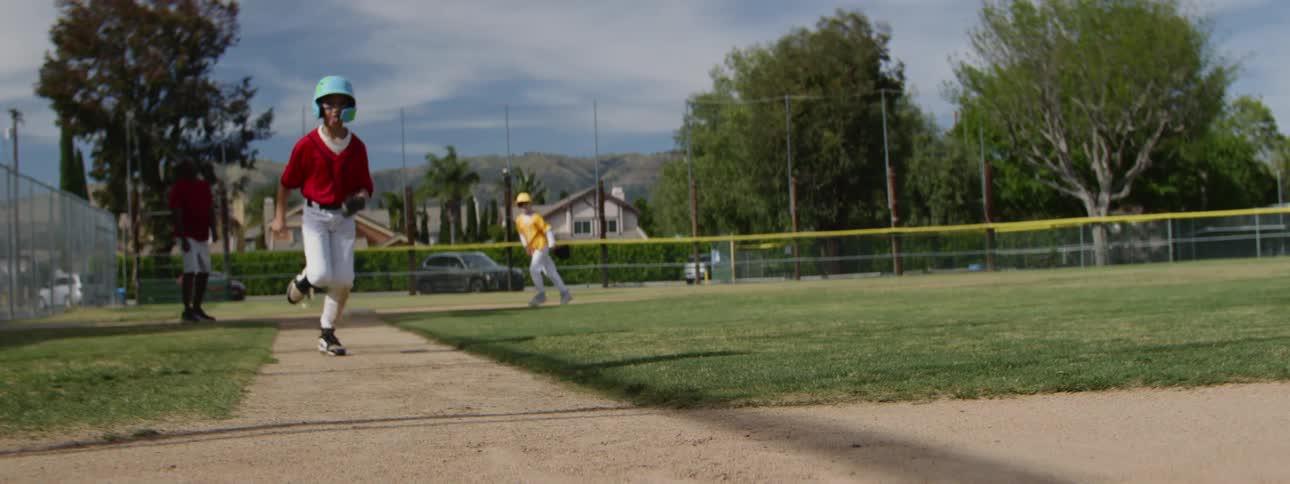 A youth baseball player runs down the baseline and slides into the base in dramatic slow motion during a game