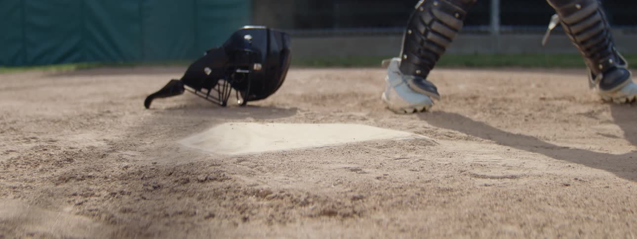 A dramatic slow-motion shot captures a baseball player in a red jersey sliding safely into home plate, kicking up a cloud of dust