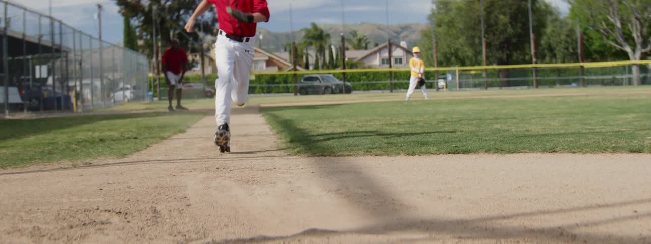 Slow motion shot of a young baseball player running toward the camera and sliding into the base, kicking up a cloud of dirt