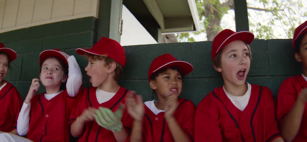Excited little league players in red uniforms cheer loudly from the dugout bench