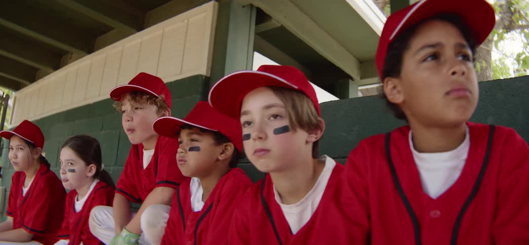 Slow motion dolly shot of a youth little league baseball team in red uniforms watching anxiously from the dugout