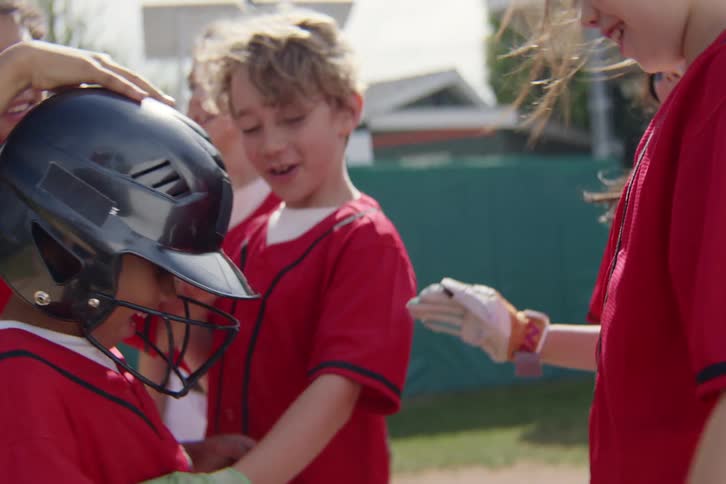 Excited young baseball players in red jerseys celebrate together in a team huddle on a sunny day