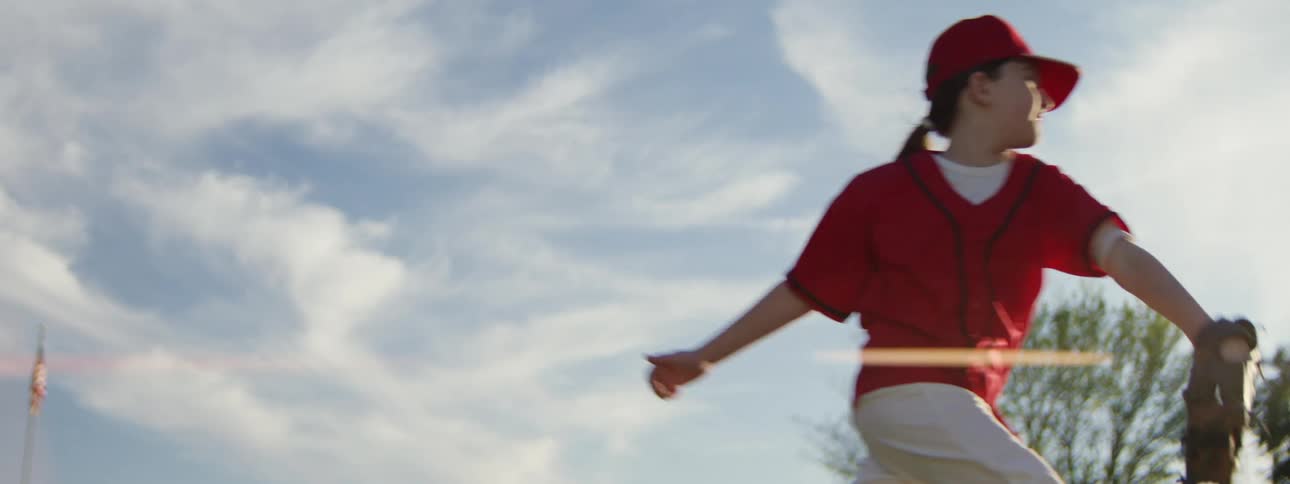A young girl in a red uniform makes a spectacular leaping catch in a game of baseball in slow motion